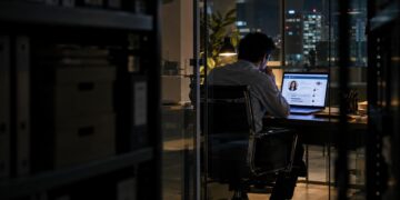 Persona desconocida consultando en secreto el perfil profesional de otra persona en una oficina después de hora