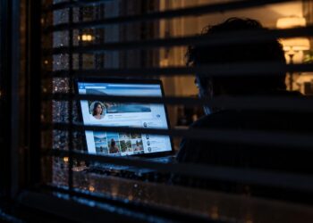 Persona desconocida observando clandestinamente un perfil de Facebook detrás de unas persianas