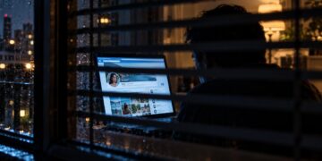 Persona desconocida observando clandestinamente un perfil de Facebook detrás de unas persianas