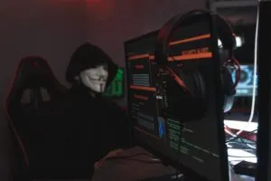 Habitación mostrando una persona usando sudadera con capucha y la máscara de Anonymous, y la pantalla de un ordenador.